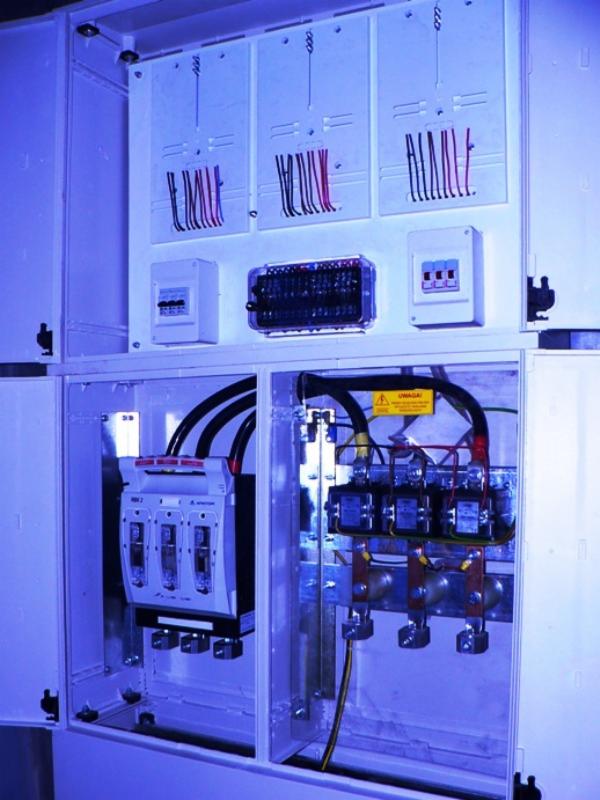 Rozdzielnica elektryczna w białej obudowie, widoczne kable, bezpieczniki i listwy zaciskowe. Detal instalacji elektrycznej wewnątrz szafy sterowniczej.