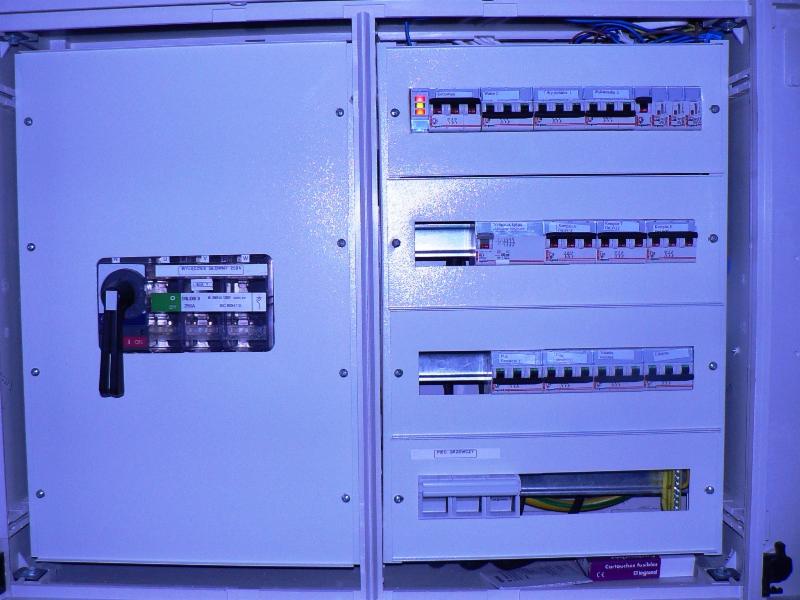 Otwarta szafa elektryczna z bezpiecznikami, wyłącznikami i okablowaniem. Widoczne oznaczenia i elementy instalacji elektrycznej wewnątrz skrzynki.