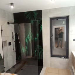 Krzysztof Kołodziejczyk - Nowoczesna kabina prysznicowa z czarnym panelem z motywem liści, szare płytki imitujące marmur, czarna armatura i okno z odbiciem osoby robiącej zdjęcie.