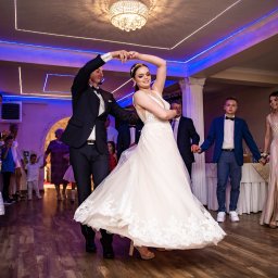 AW Fotografia Alicja Węgrzyn - Pierwszy taniec pary młodej w sali z dekoracjami świetlnymi, goście weselni w tle.