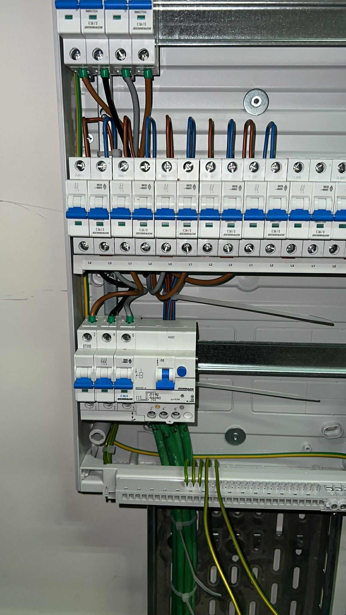 Rozdzielnica elektryczna Schrack z zainstalowanymi bezpiecznikami i przewodami. Widoczne kable w kolorach: zielono-żółtym, brązowym i niebieskim.