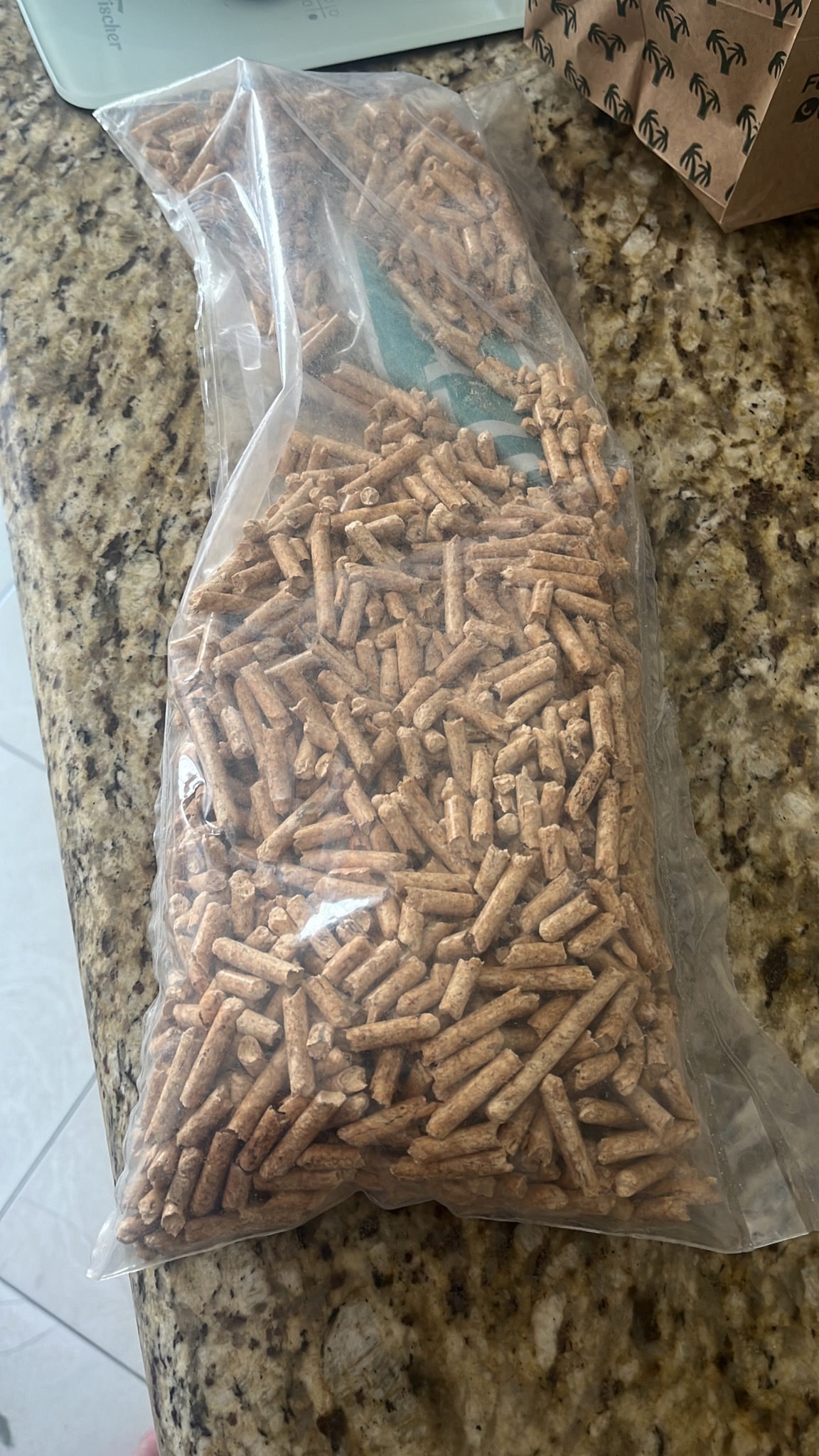 Worek przezroczysty wypełniony brązowymi granulkami na tle marmurowego blatu.