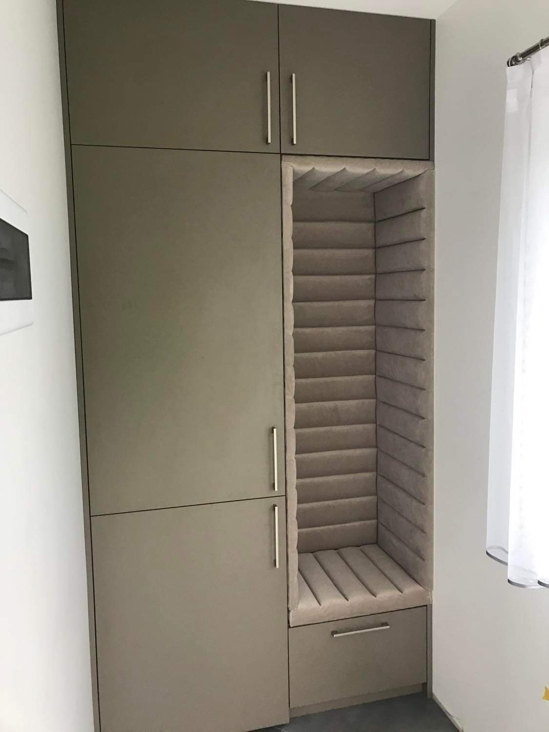 Wnęka w zabudowie meblowej z tapicerowanym siedziskiem i oparciem w pionowe pasy, szara kolorystyka.