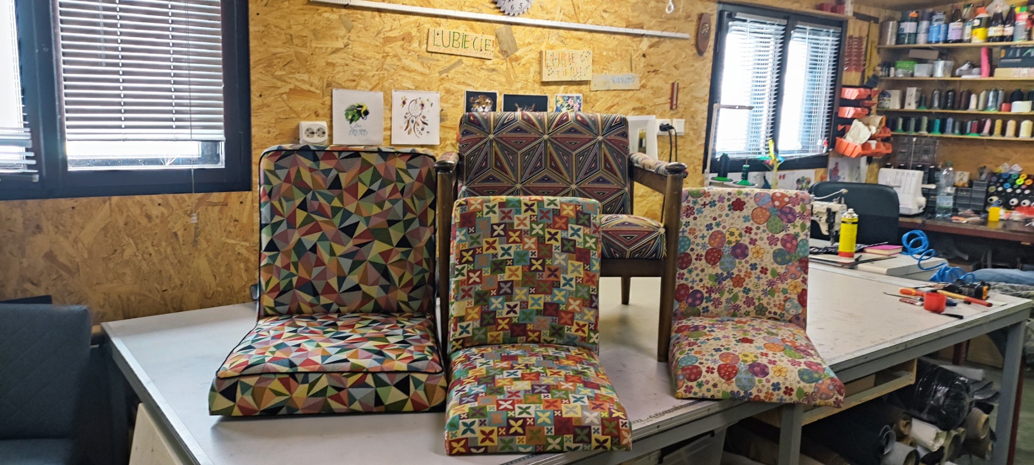 Odnowione krzesła z różnymi wzorami tapicerki, ustawione w warsztacie z drewnianymi ścianami i narzędziami w tle.