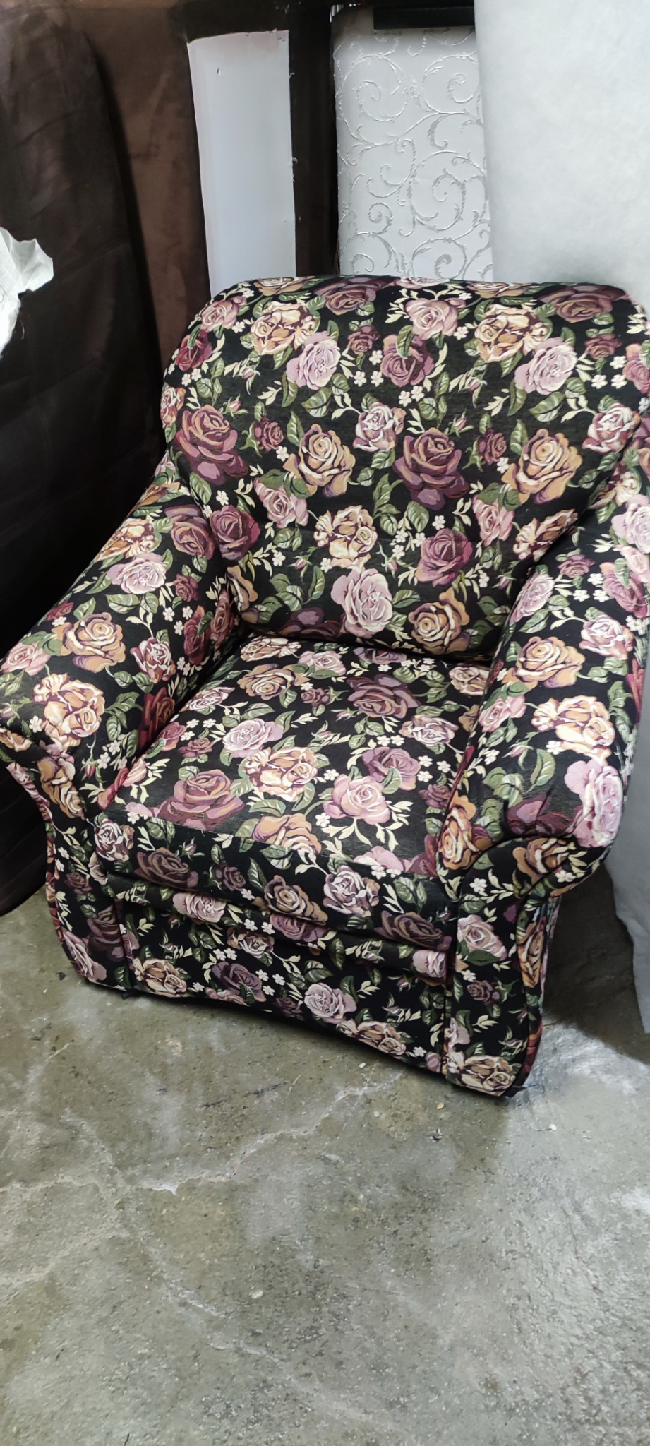 Krótki fotel klubowy z podłokietnikami, obity ciemną tkaniną w motywy róż i liści, sfotografowany z góry na tle betonowej podłogi.