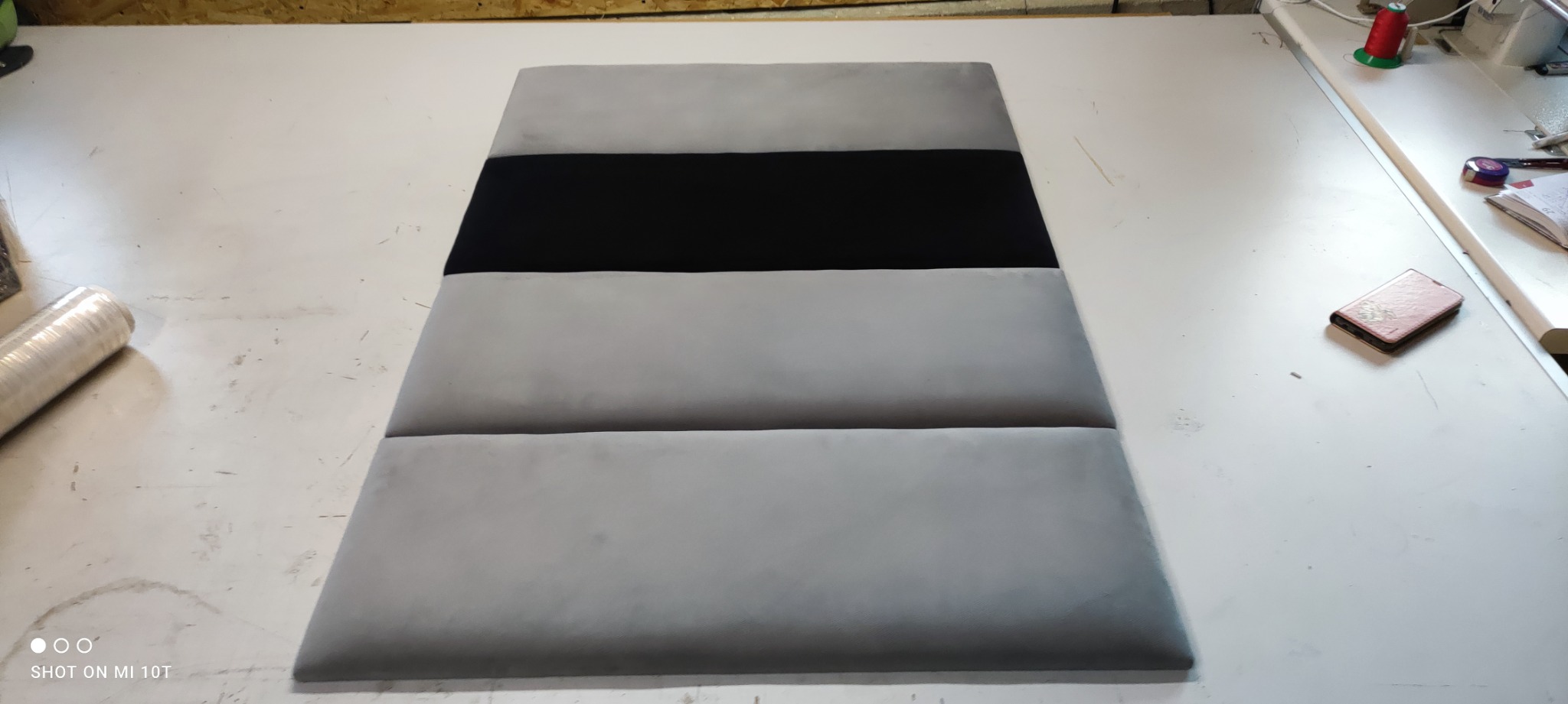 Panel tapicerowany z trzema poziomymi pasami: szarym, czarnym i szarym, leżący na białym stole.