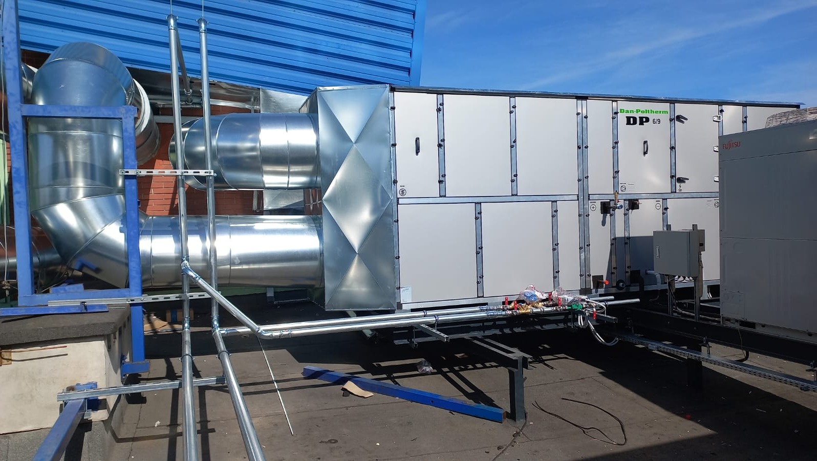 Instalacja przemysłowej klimatyzacji Dan-Poltherm DP 6/9 z rurami wentylacyjnymi na dachu budynku, widoczny również agregat Fujitsu.