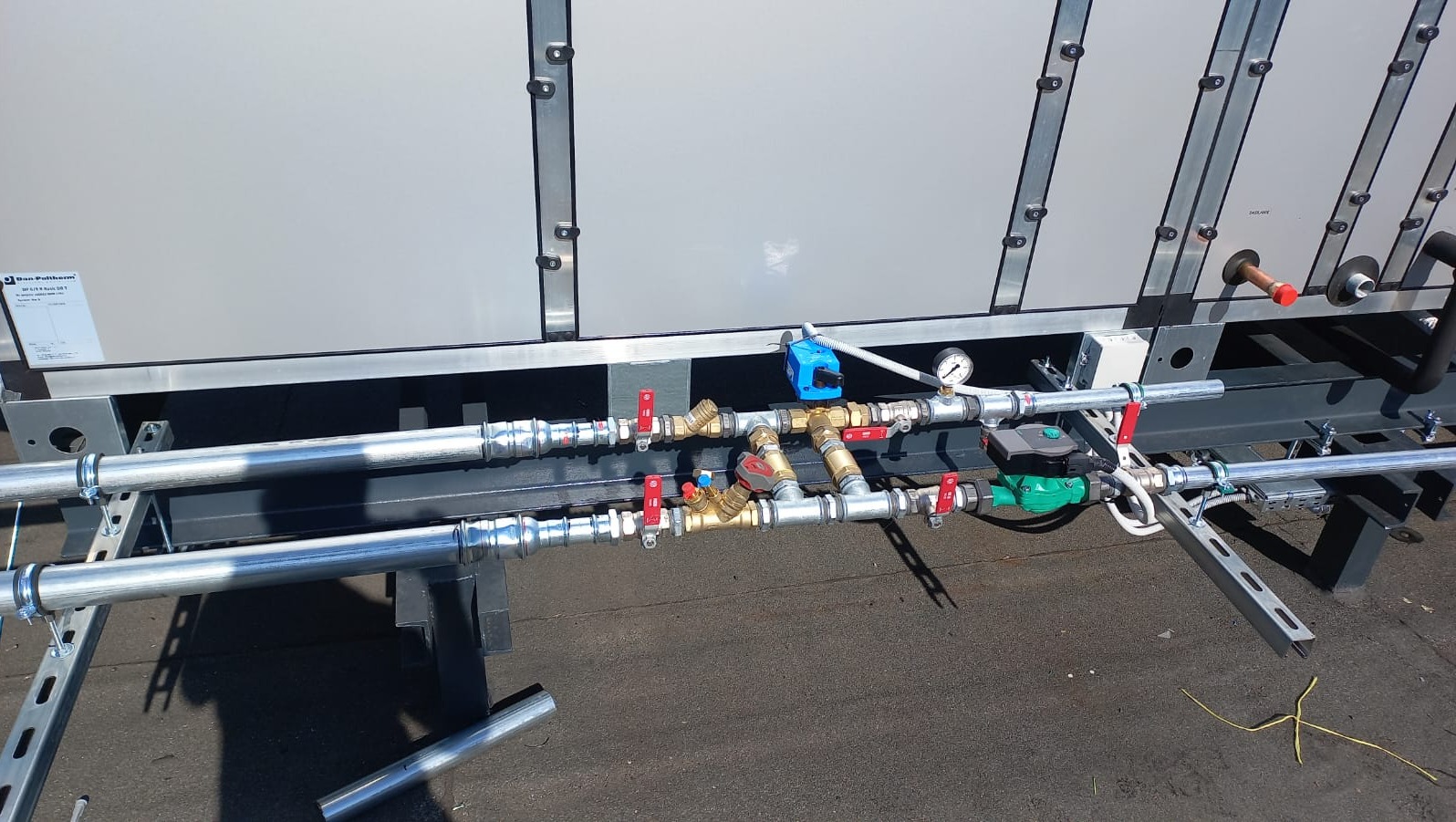 Zewnętrzna instalacja rur i zaworów klimatyzacji przemysłowej, widoczne manometry, zawory z czerwonymi uchwytami, metalowe rury i elementy mocujące.