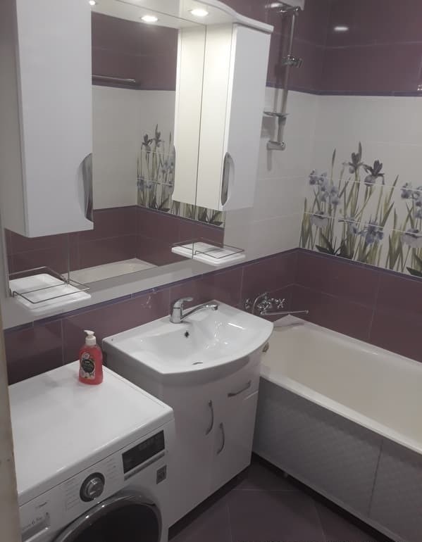 Łazienka po remoncie z umywalką na szafce, pralką obok, wanną i białymi szafkami wiszącymi, ściany wyłożone kafelkami z motywem kwiatowym i bordiurą.