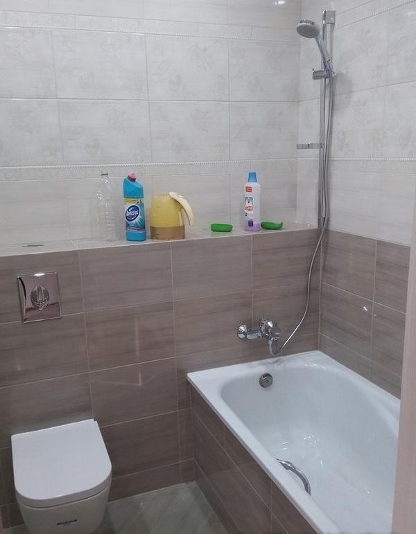 Nowoczesna łazienka z wanną, prysznicem, toaletą i półką z chemią gospodarczą, wykończona w beżowych i białych płytkach.