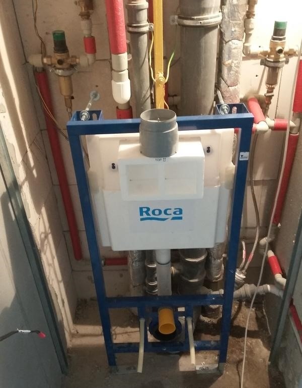 Stelaż podtynkowy WC marki Roca zamontowany w surowym wnętrzu, widoczne rury instalacyjne i zawory.