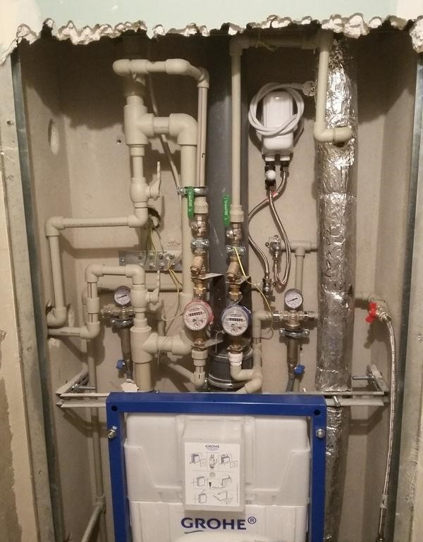 Instalacja wodno-kanalizacyjna w zabudowie, widoczne liczniki wody, zawory, rury z izolacją oraz zbiornik podtynkowy marki Grohe przed zakryciem płytami.