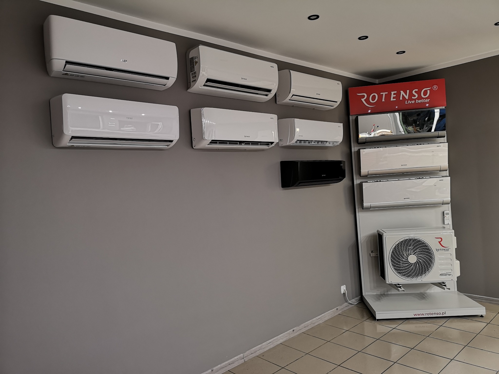 Ekspozycja klimatyzatorów różnych modeli i marek, w tym Rotenso, zamontowanych na ścianie i na stojaku prezentacyjnym w showroomie.