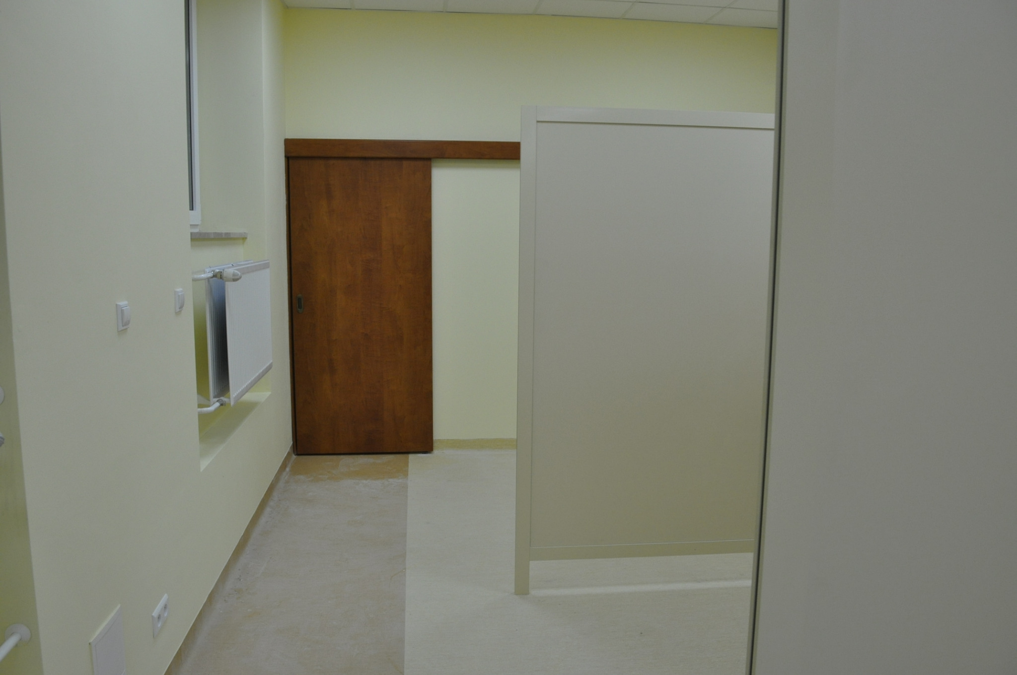 Wnętrze biura po remoncie: widoczna drewniana, przesuwna brama, biały grzejnik pod oknem i ścianka działowa.