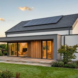 ATO-ARCHITEKTURA - Nowoczesny dom z panelami słonecznymi na dachu, widok z ogrodu. Duże przeszklenia, drewniane elementy elewacji, zadbany trawnik i roślinność.