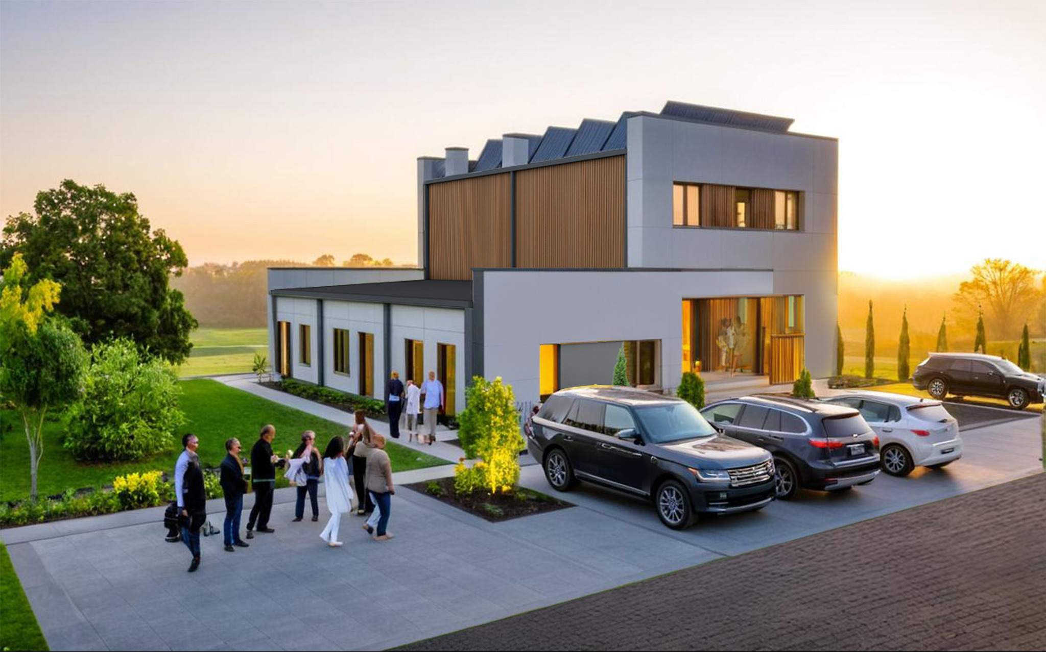 Nowoczesny dom z płaskim dachem i drewnianą elewacją, oświetlony ciepłym światłem zachodzącego słońca. Przed budynkiem zaparkowane samochody i grupa osób.