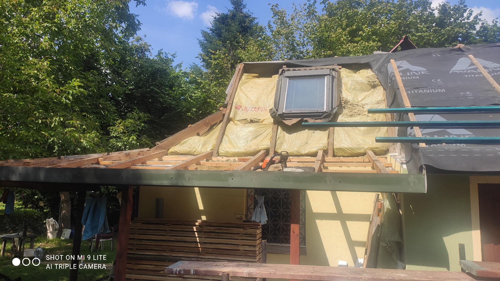 Remont dachu z oknem dachowym: widoczne krokwie, izolacja z folią JUTAFOL, membrana dachowa LINE TITANIUM i piła spalinowa STIHL na tle zieleni.