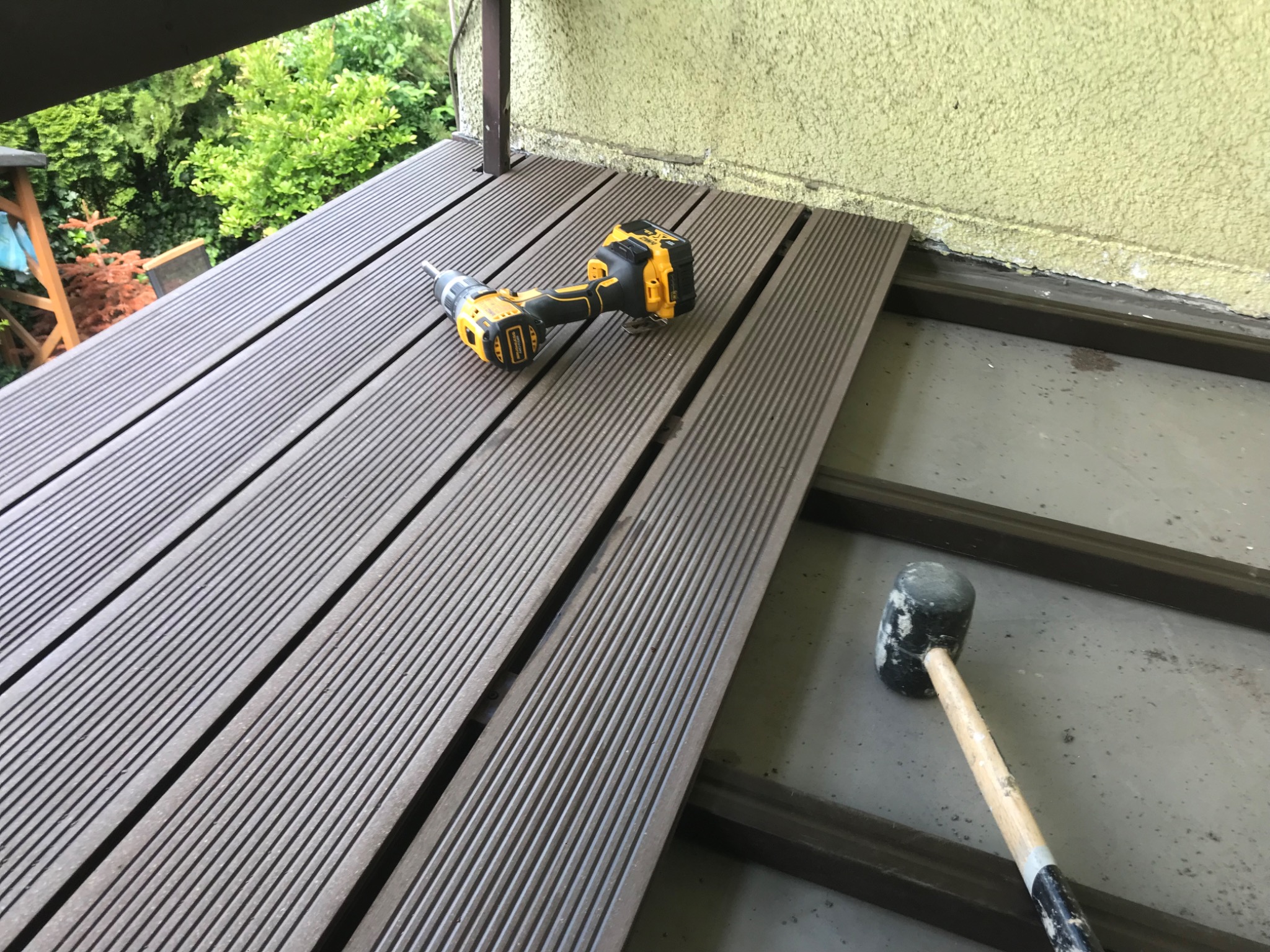 Montaż kompozytowej deski podłogowej na balkonie, widoczna wkrętarka DeWalt i gumowy młotek, częściowo ułożona podłoga z widoczną konstrukcją wsporczą.