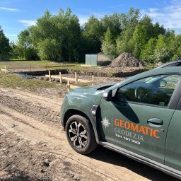 Geomatic Geodezja Mateusz Laskowski - Geodezyjne wytyczenie fundamentów pod budowę domu, widoczny samochód terenowy z logo firmy Geomatic Geodezja, w tle drzewa i niebieski wąż do pomiarów.