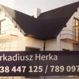 Wizytówka firmy budowlanej Arkadiusz Herka z numerami telefonów, na tle domu w trakcie prac elewacyjnych, z widocznymi rusztowaniami.