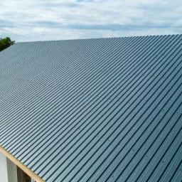 Nowy, blaszany dach w kolorze grafitowym z wyraźnymi żłobieniami, zamontowany na nowo wybudowanym domu z białymi ścianami, widok z góry.