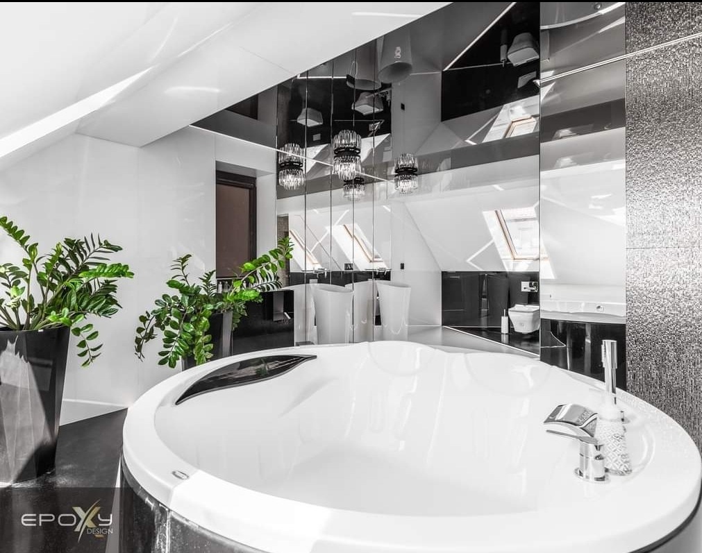 Nowoczesna łazienka na poddaszu w czerni i bieli z okrągłą wanną, lustrzanym sufitem, wiszącymi lampami, roślinami doniczkowymi i błyszczącą mozaiką na ścianie.