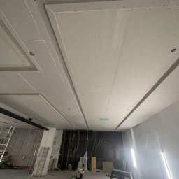 Finish line - Sufit podwieszany z płyt gipsowo-kartonowych z ozdobnymi wnękami i listwami, w trakcie montażu, widoczne narzędzia i materiały budowlane.