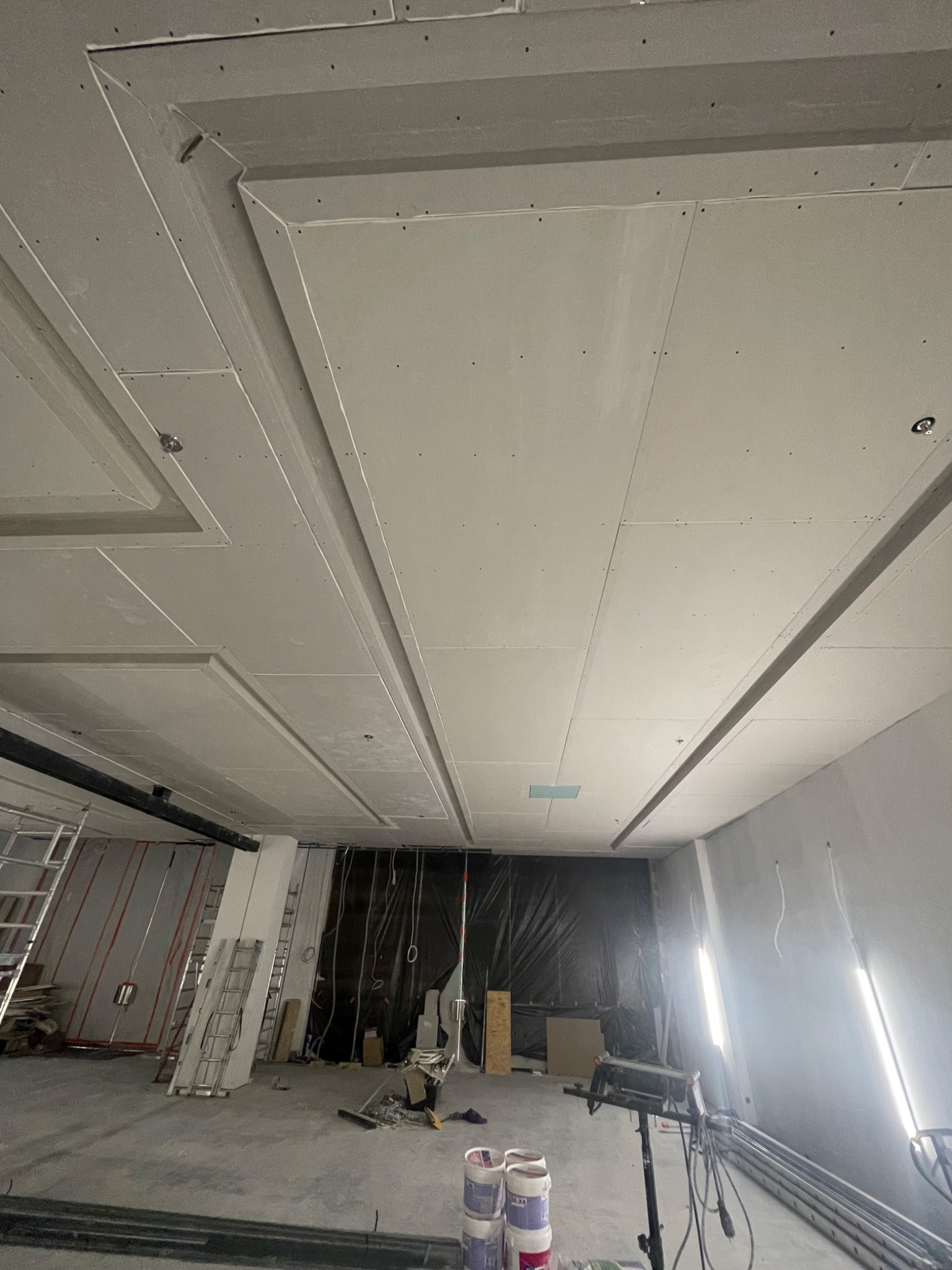 Sufit podwieszany z płyt gipsowo-kartonowych z ozdobnymi wnękami i listwami, w trakcie montażu, widoczne narzędzia i materiały budowlane.