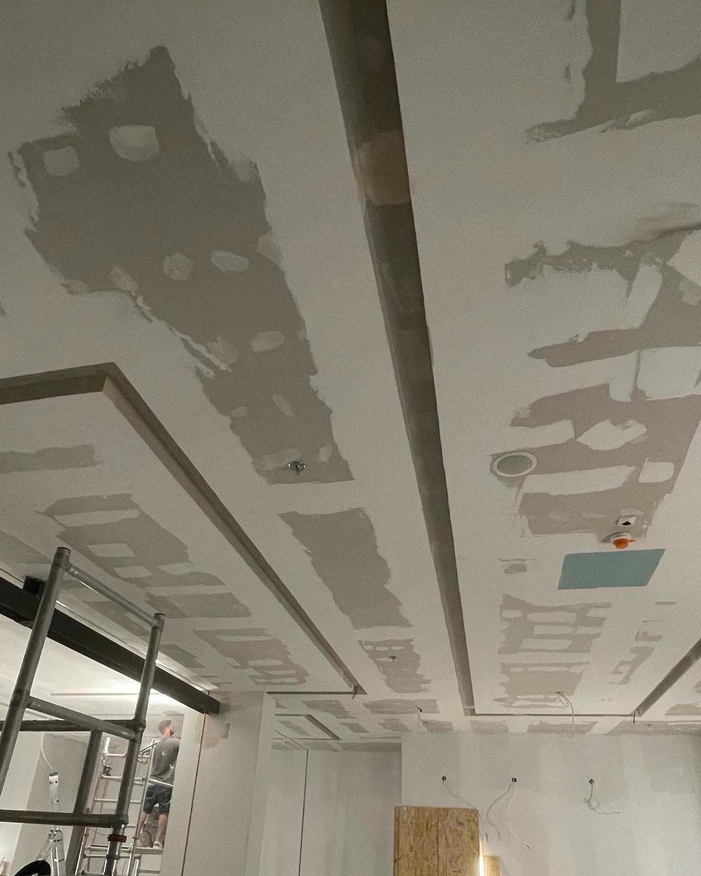 Sufit podwieszany z płyt gipsowo-kartonowych w trakcie szpachlowania, widoczne profile i oświetlenie, drabina w tle.