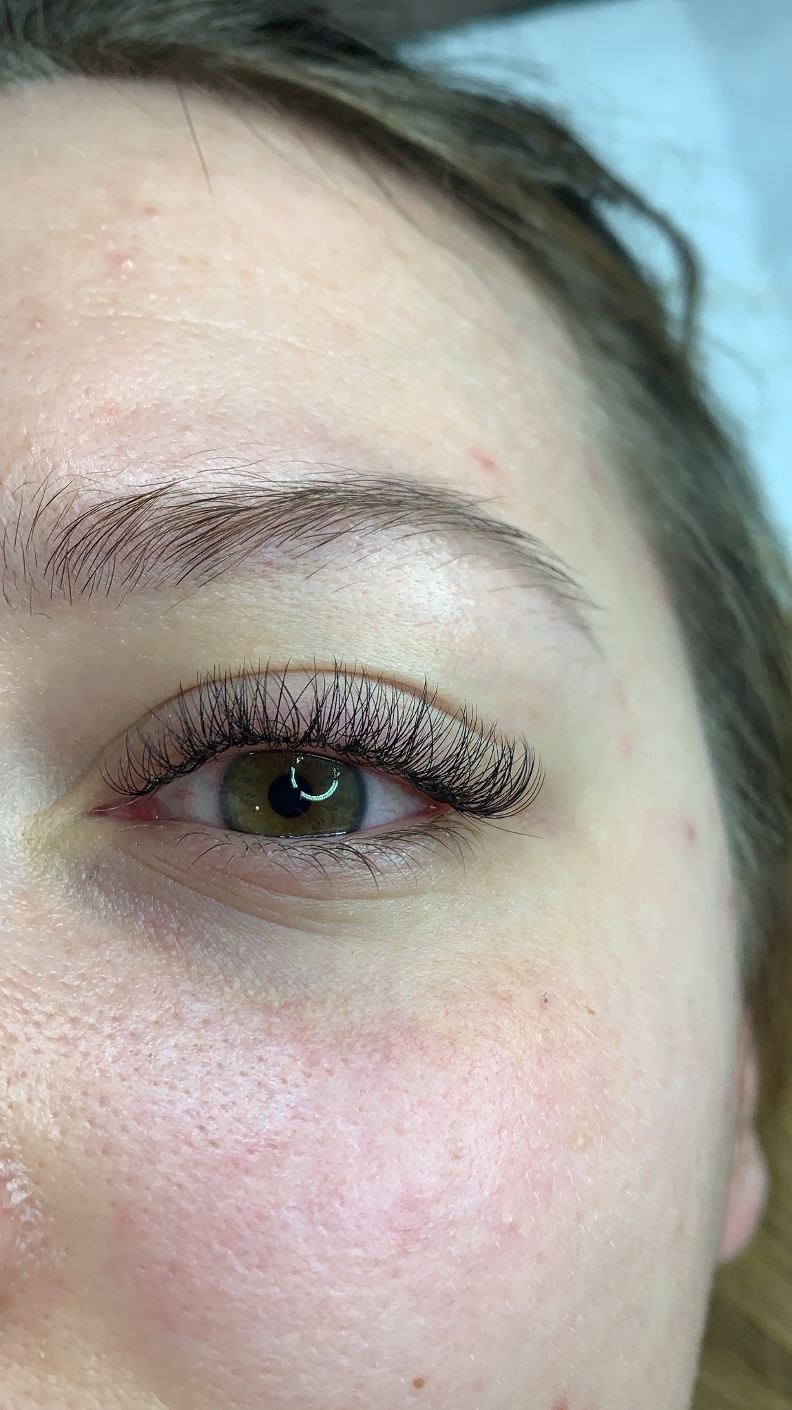 Zbliżenie na oko kobiety z profesjonalnie przedłużonymi rzęsami, widoczny delikatny makijaż brwi i zielona tęczówka.
