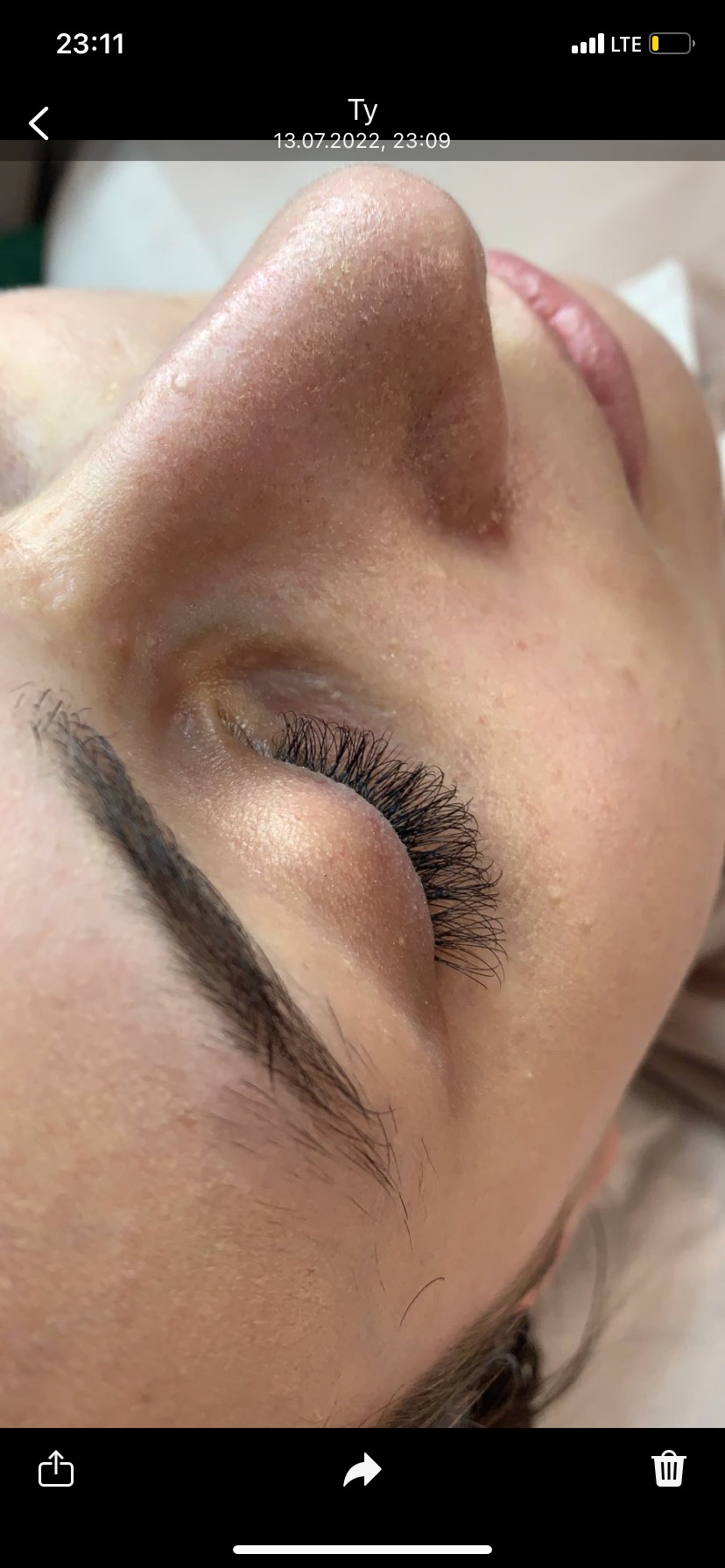 Zbliżenie na oko kobiety po zabiegu przedłużania rzęs, widoczne pojedyncze włoski brwi i drobne niedoskonałości skóry