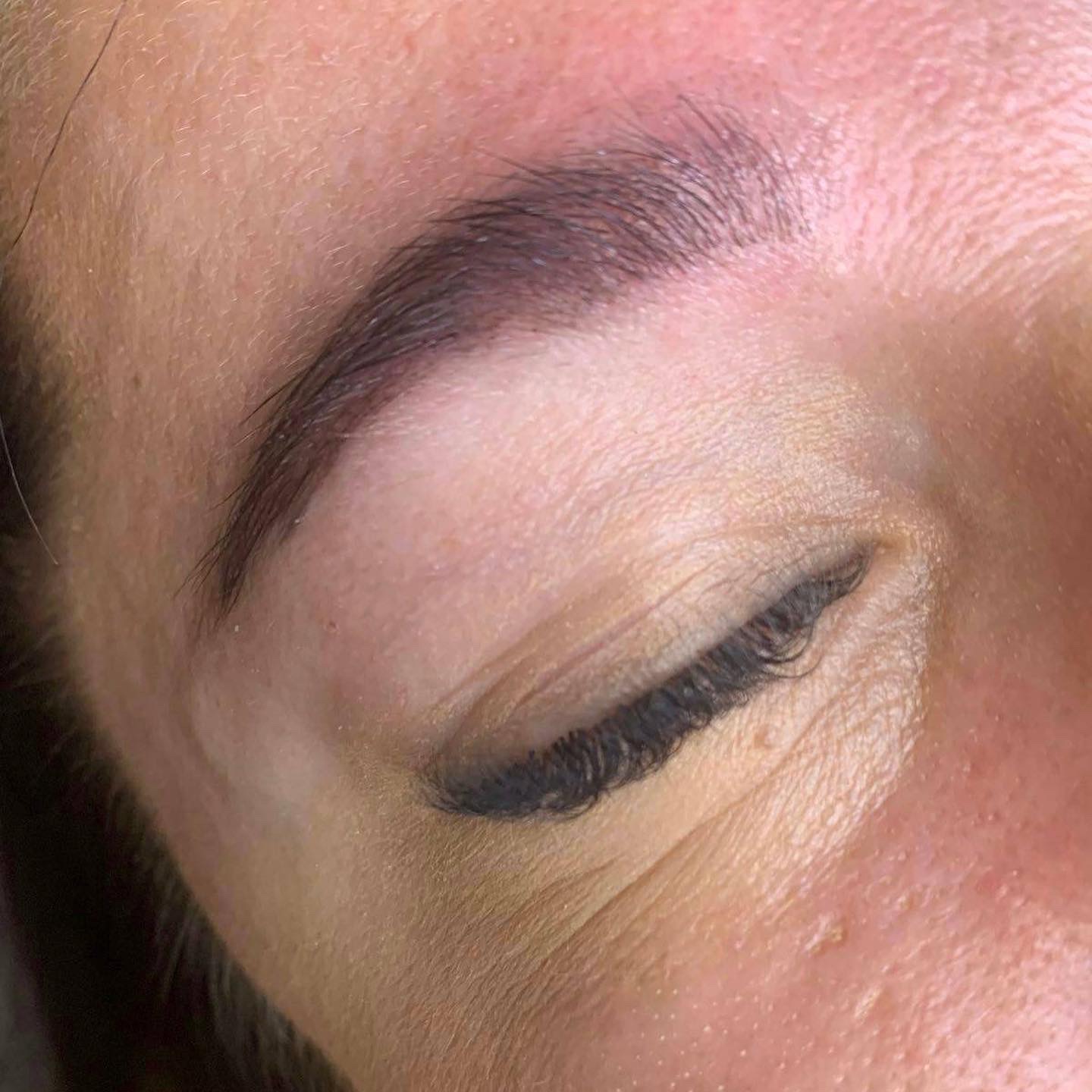 Zbliżenie na oko z idealnie wystylizowanymi, ciemnymi brwiami po zabiegu henny lub microbladingu, widoczne delikatne zmarszczki wokół oka.