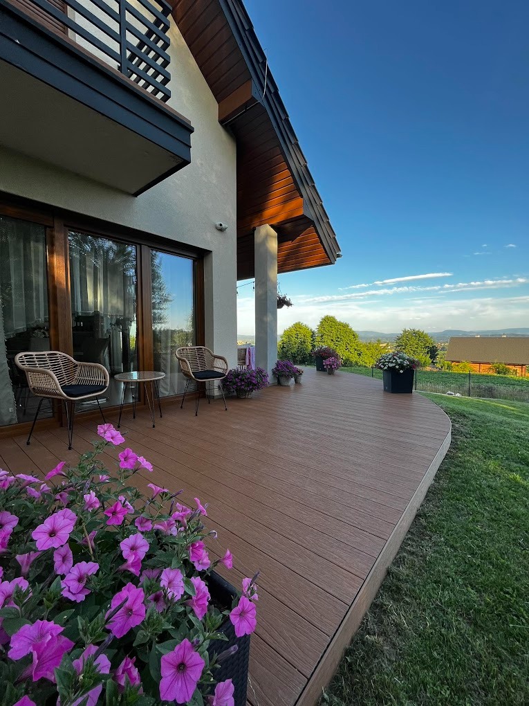 Nowoczesny taras kompozytowy z widokiem na Krzeszowice, wyposażony w rattanowe krzesła i stolik, ozdobiony kwiatami w donicach.