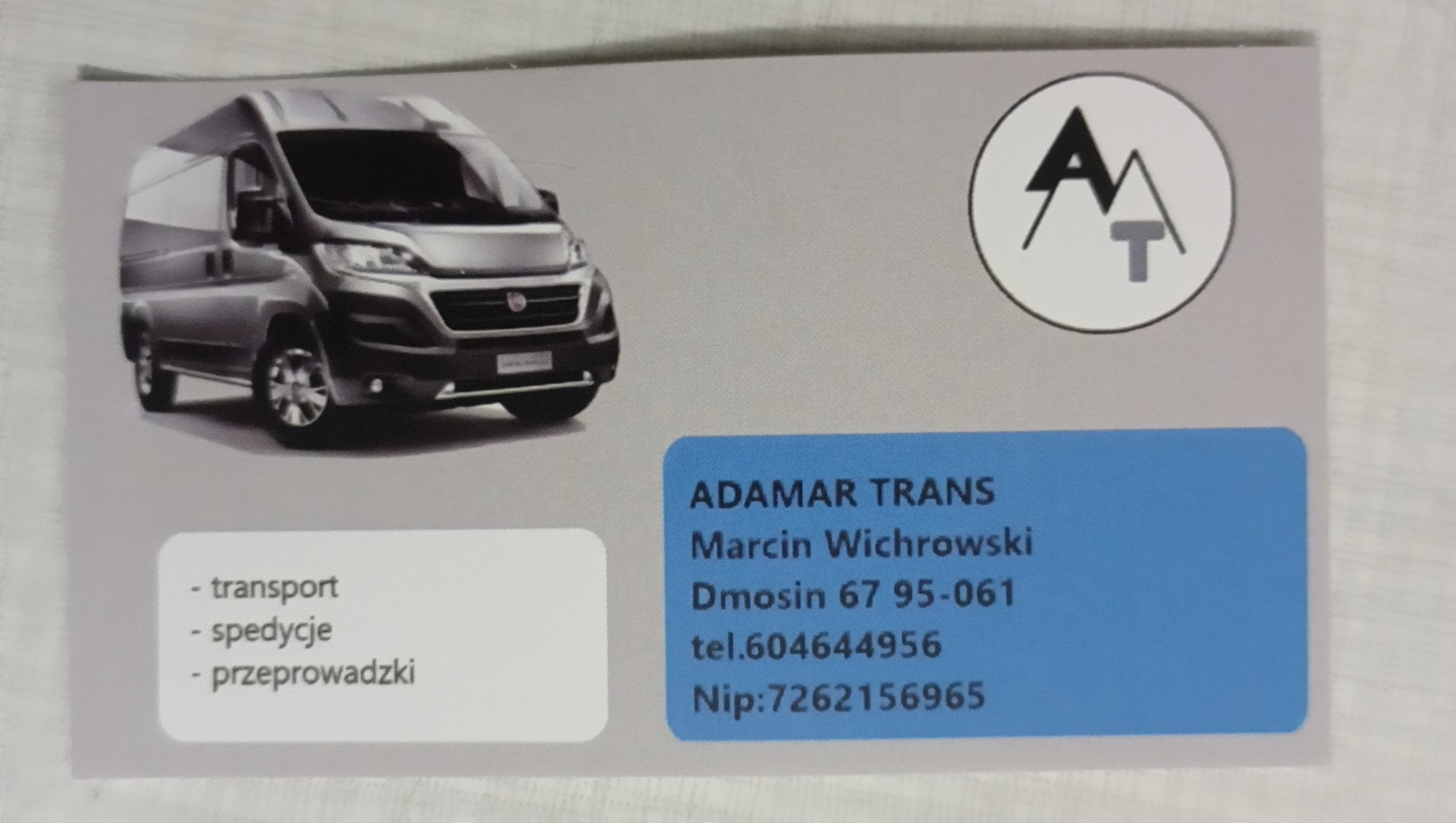 Wizytówka firmy transportowej Adamar Trans z ilustracją szarego busa, logo z literami A i T, adresem i numerem telefonu.