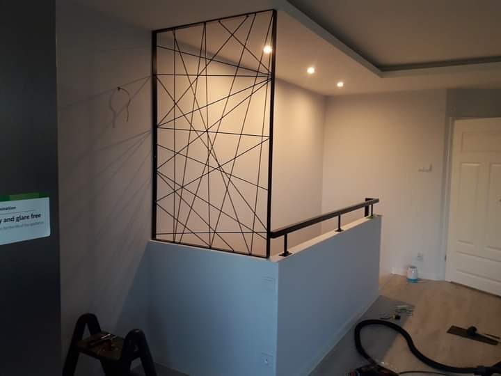 Metalowa konstrukcja z abstrakcyjnym wzorem linii, pełniąca funkcję balustrady na antresoli w nowoczesnym wnętrzu.