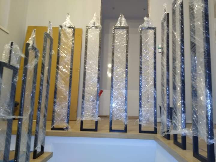 Elementy balustrady schodowej, zabezpieczone folią, przygotowane do montażu w Białymstoku. Czarne, metalowe słupki o różnych kształtach górnej części, czekają na instalację.