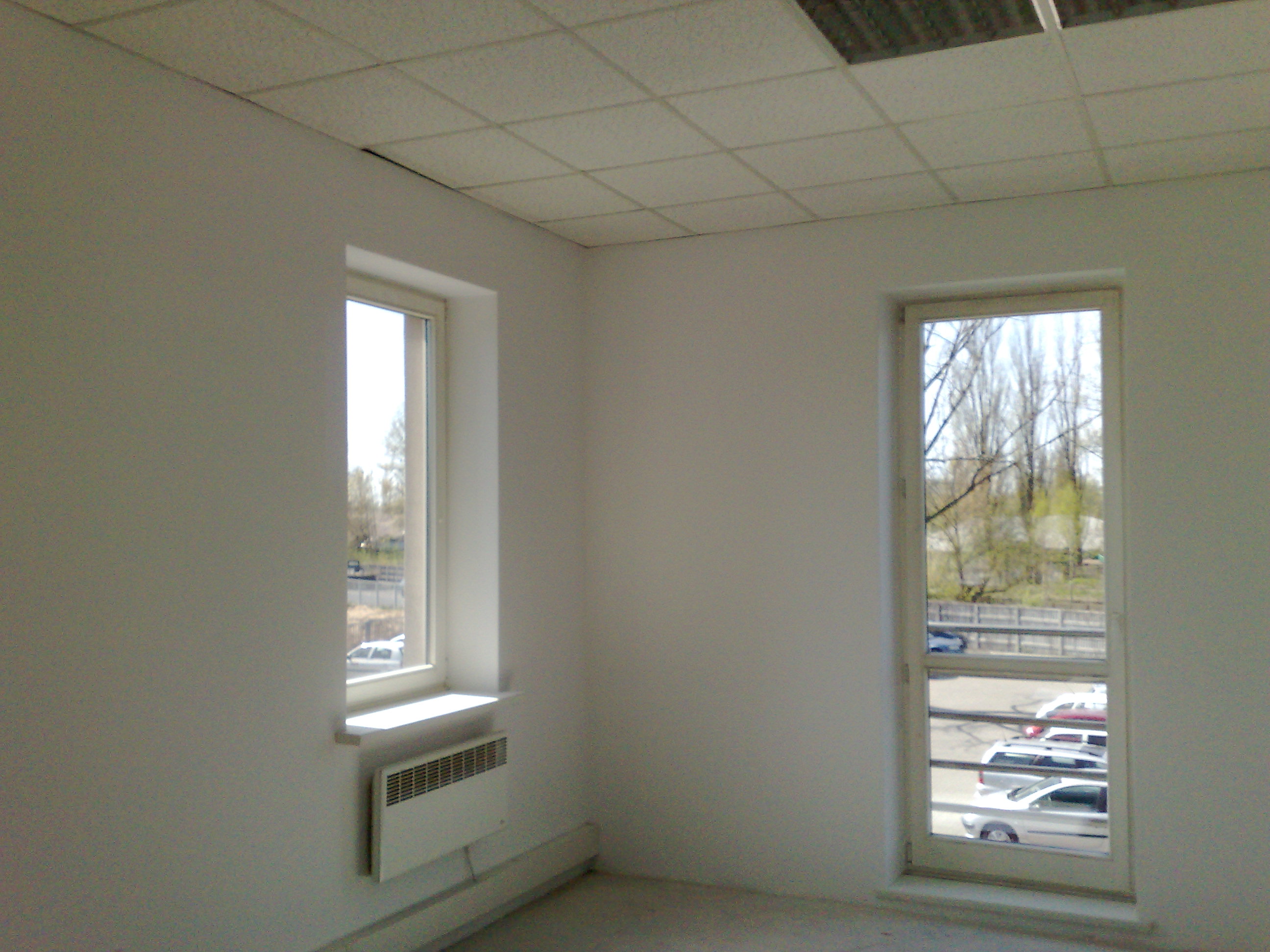 Puste, jasne pomieszczenie w Warszawie z dwoma oknami, grzejnikiem pod jednym z nich i kasetonowym sufitem, przygotowane do prac wykończeniowych.