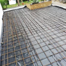 Przygotowanie zbrojenia na czarnej folii, prawdopodobnie pod wylewkę betonową tarasu lub balkonu, widoczne elementy szalunku i materiały budowlane w tle.