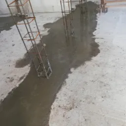 Wylewanie betonu wokół stalowych zbrojeń słupów na surowym betonowym podłożu w trakcie budowy.