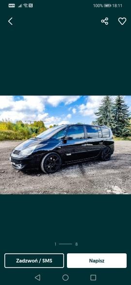 Czarny, błyszczący van Renault Espace z czarnymi felgami stoi na żwirowym podłożu; w tle drzewa i błękitne niebo z chmurami.