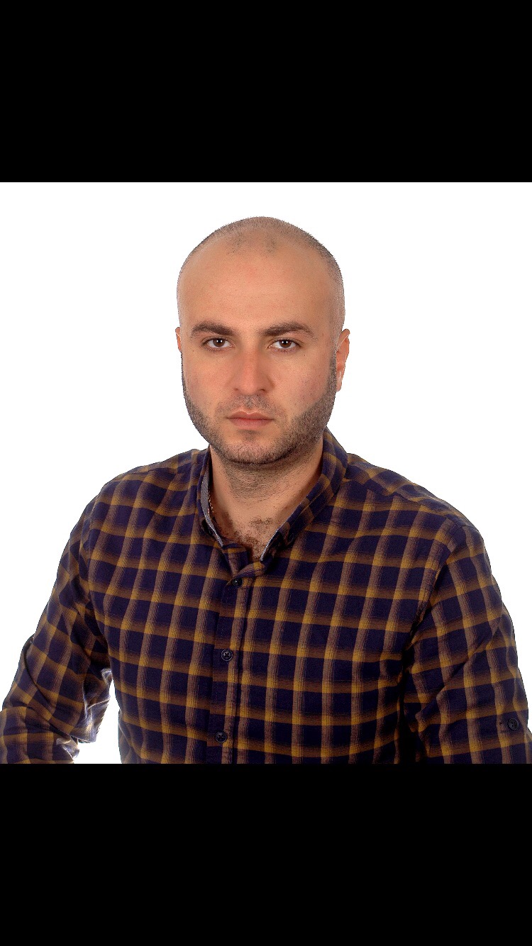 Portret mężczyzny z krótką brodą, ubranego w koszulę w kratę, na białym tle.