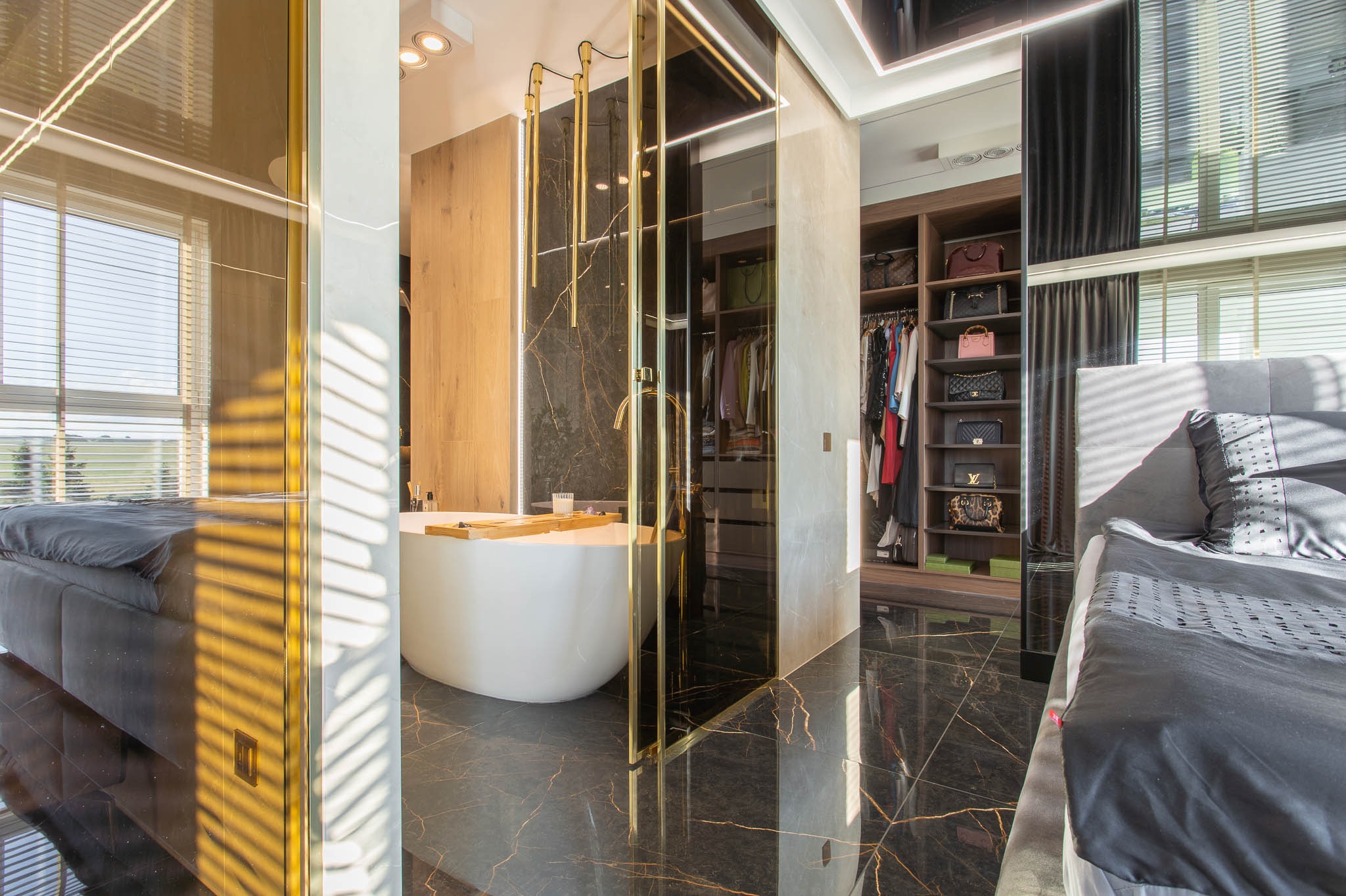 Luksusowa sypialnia z wanną wolnostojącą, garderobą i czarną marmurową podłogą z złotymi żyłami, widoczna przez szklane drzwi z złotymi ramami.