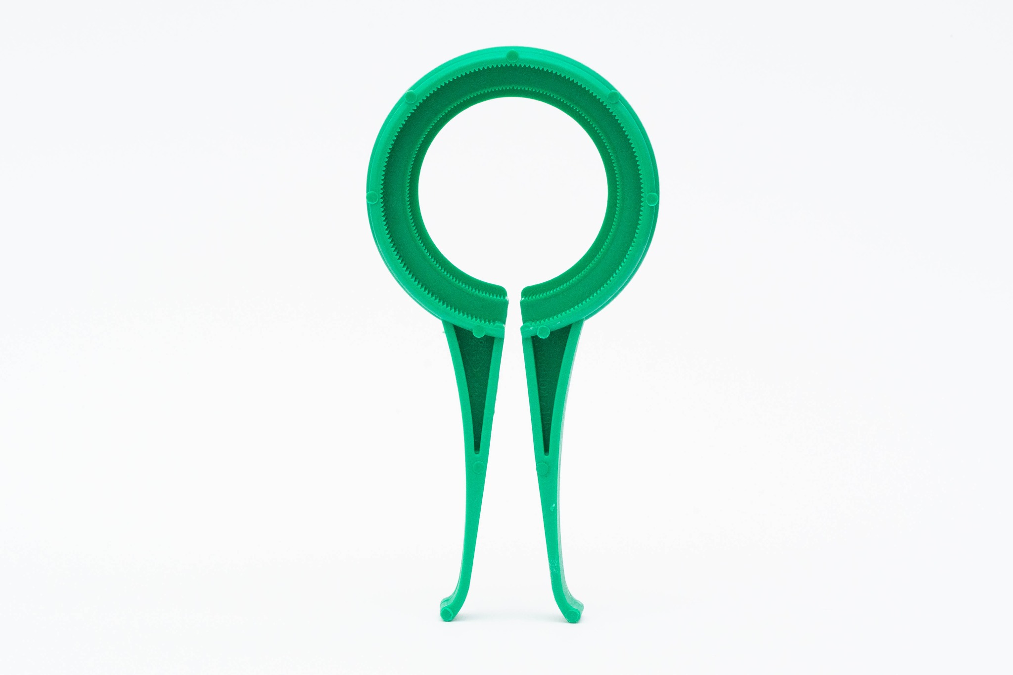 Zielony, plastikowy otwieracz do słoików z ząbkowanym pierścieniem i uchwytami, na białym tle.