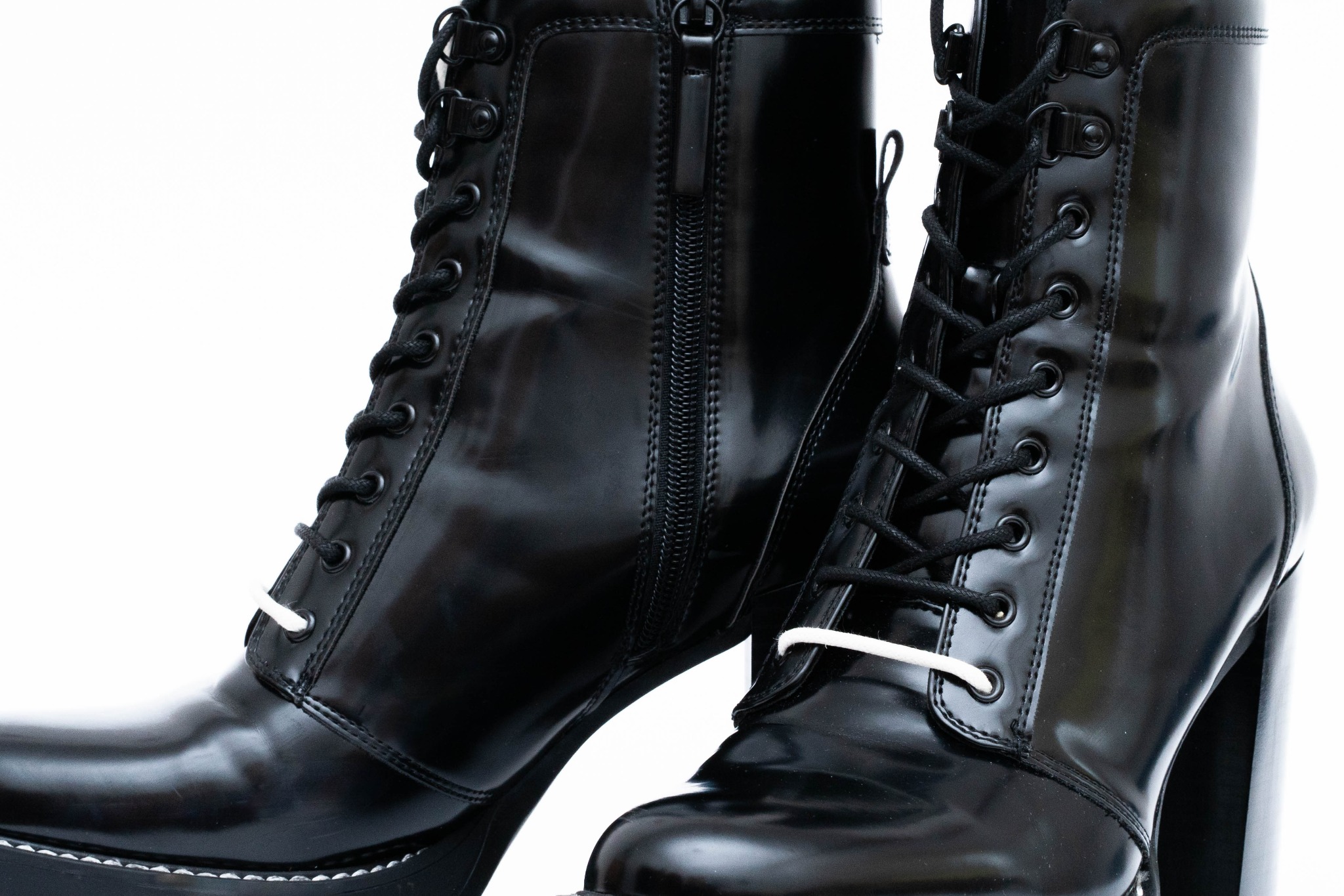 Para czarnych, lakierowanych botków na wysokim obcasie, sznurowanych z przodu i zapinanych na zamek z boku, na białym tle.