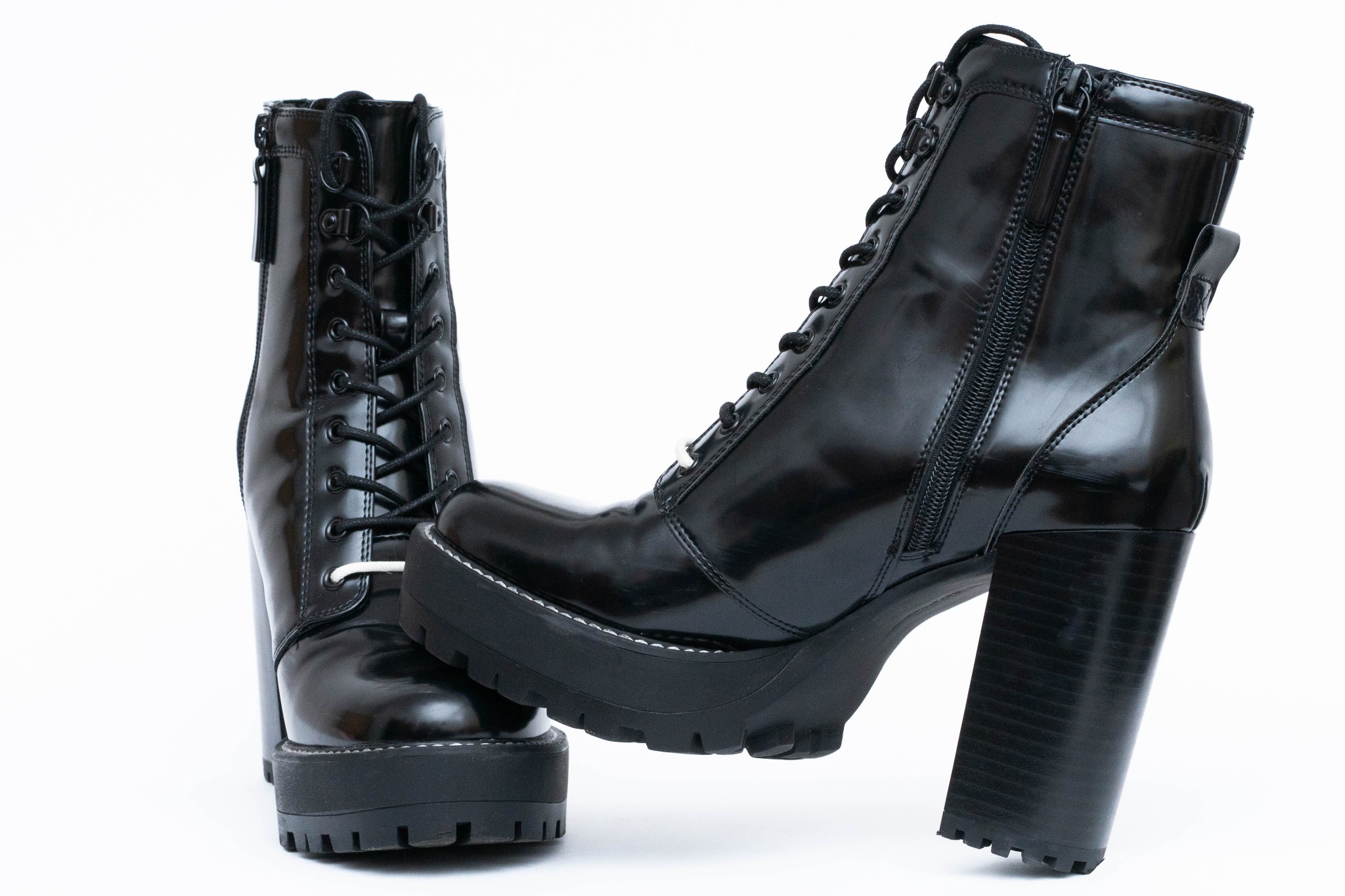 Para czarnych, lakierowanych botków na platformie i wysokim, grubym obcasie, sznurowane i zapinane na zamek, na białym tle.
