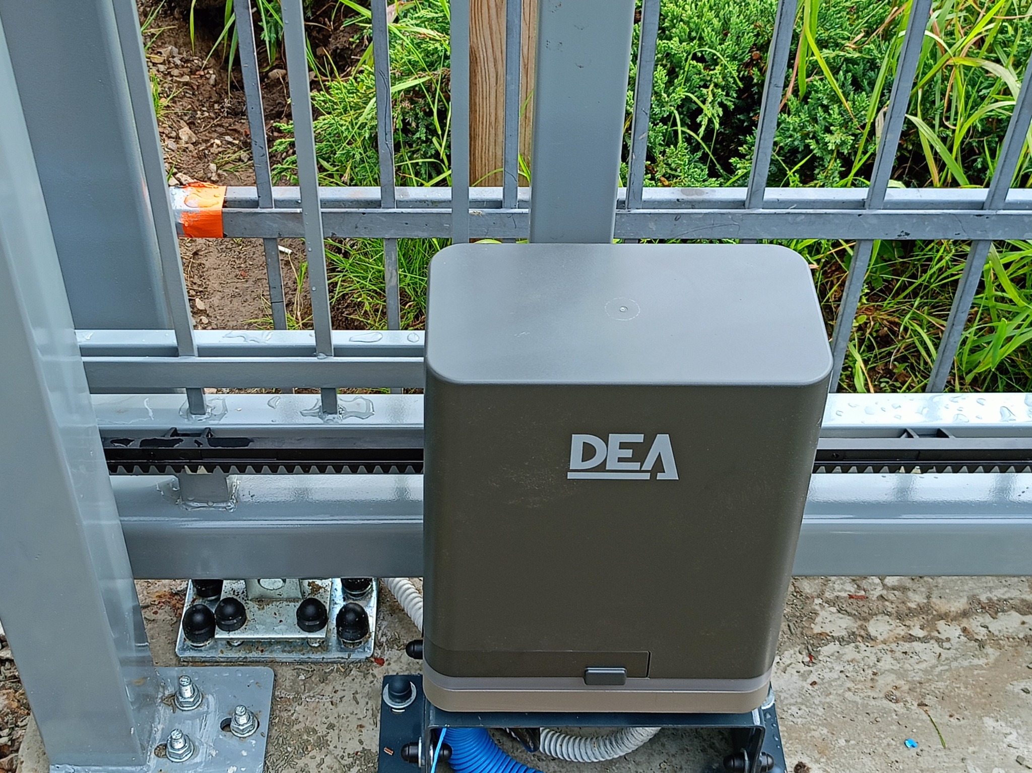 Zamontowany napęd DEA przy bramie przesuwnej w Zamościu. Widoczna listwa zębata i elementy mocujące. Ujęcie z bliska, zieleń w tle.