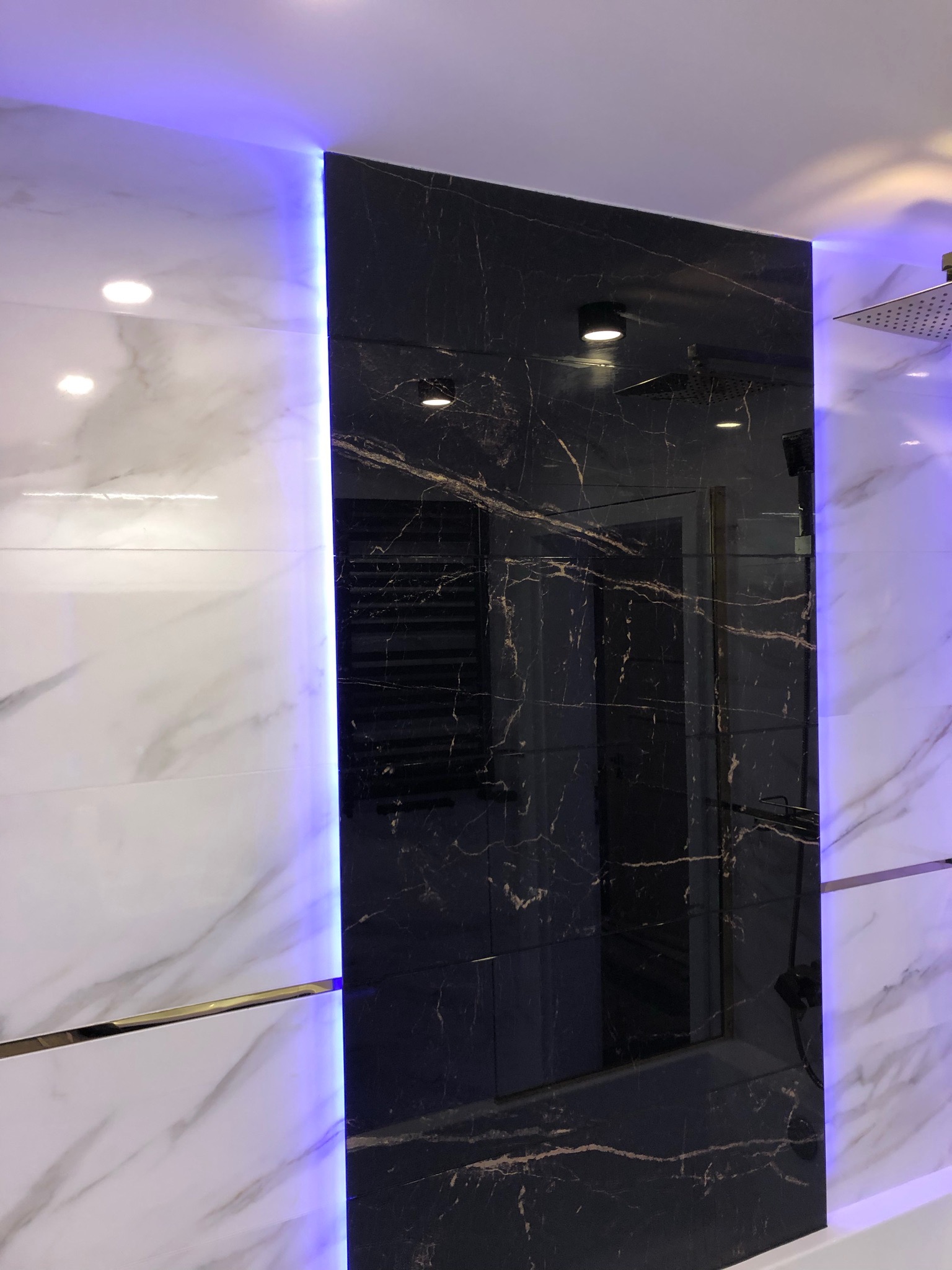 Nowoczesna łazienka z czarno-białymi marmurowymi płytkami, oświetleniem LED i deszczownicą.