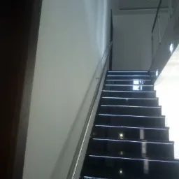 Nowoczesne, czarne schody z podświetleniem LED, z metalową poręczą, widok z dołu, przy białej ścianie i ciemnych drzwiach.