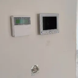 Panel alarmowy Satel Integra i wideodomofon Akuvox zamontowane na ścianie, widoczne gniazdko elektryczne bez osprzętu.