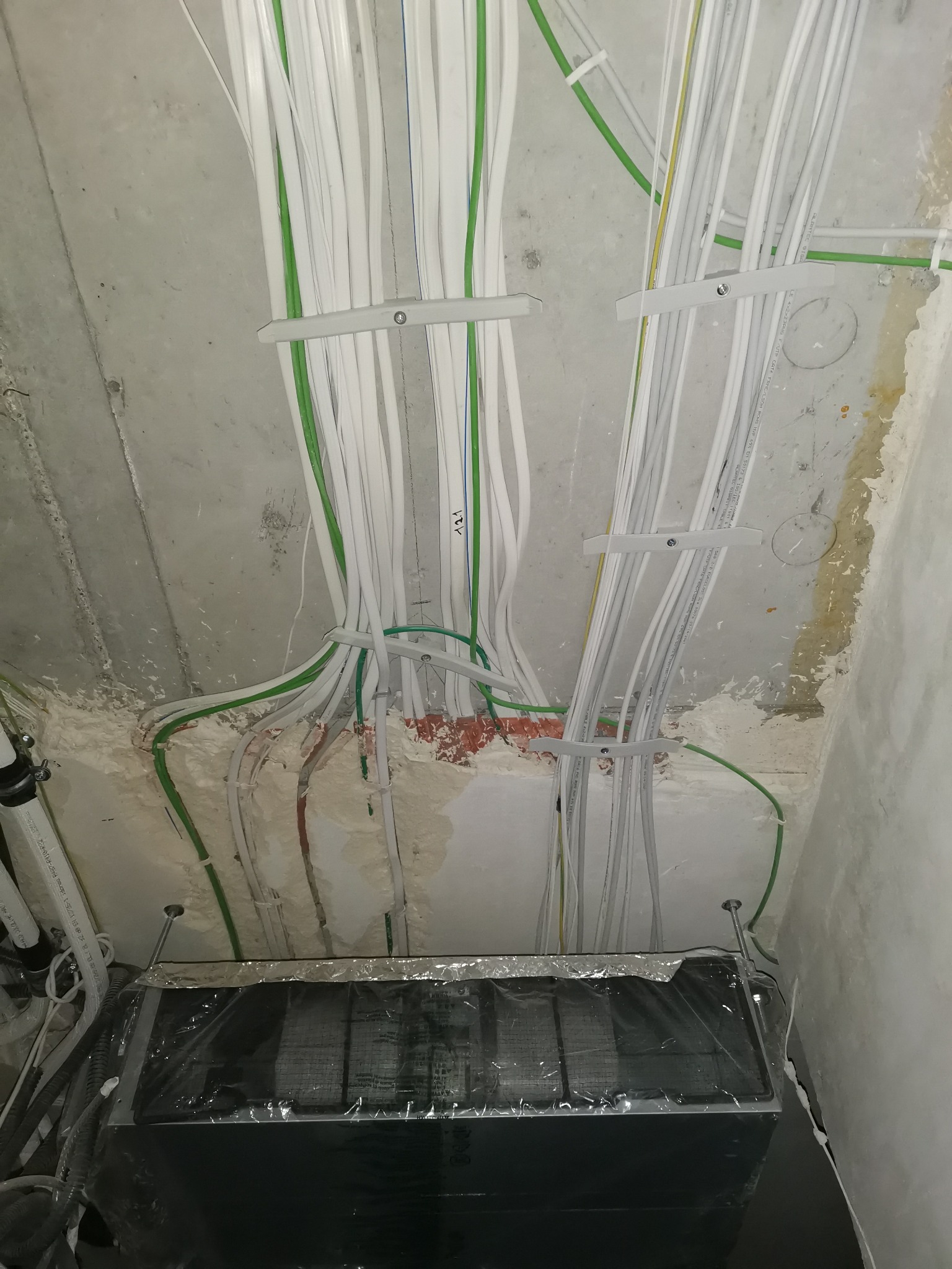 Wiązki kabli elektrycznych w peszlach i korytach mocowanych do sufitu, widoczne ślady po pracach wykończeniowych na suficie i ścianach.